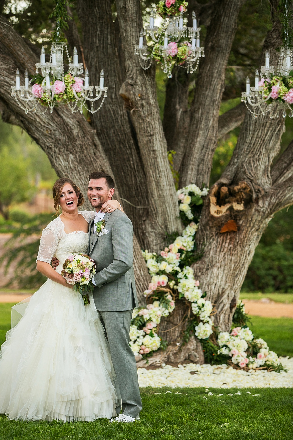 Dancing Apache Lodge wedding with bride and groom posing for a photo in front of a tree covered in flowers and chandeliers