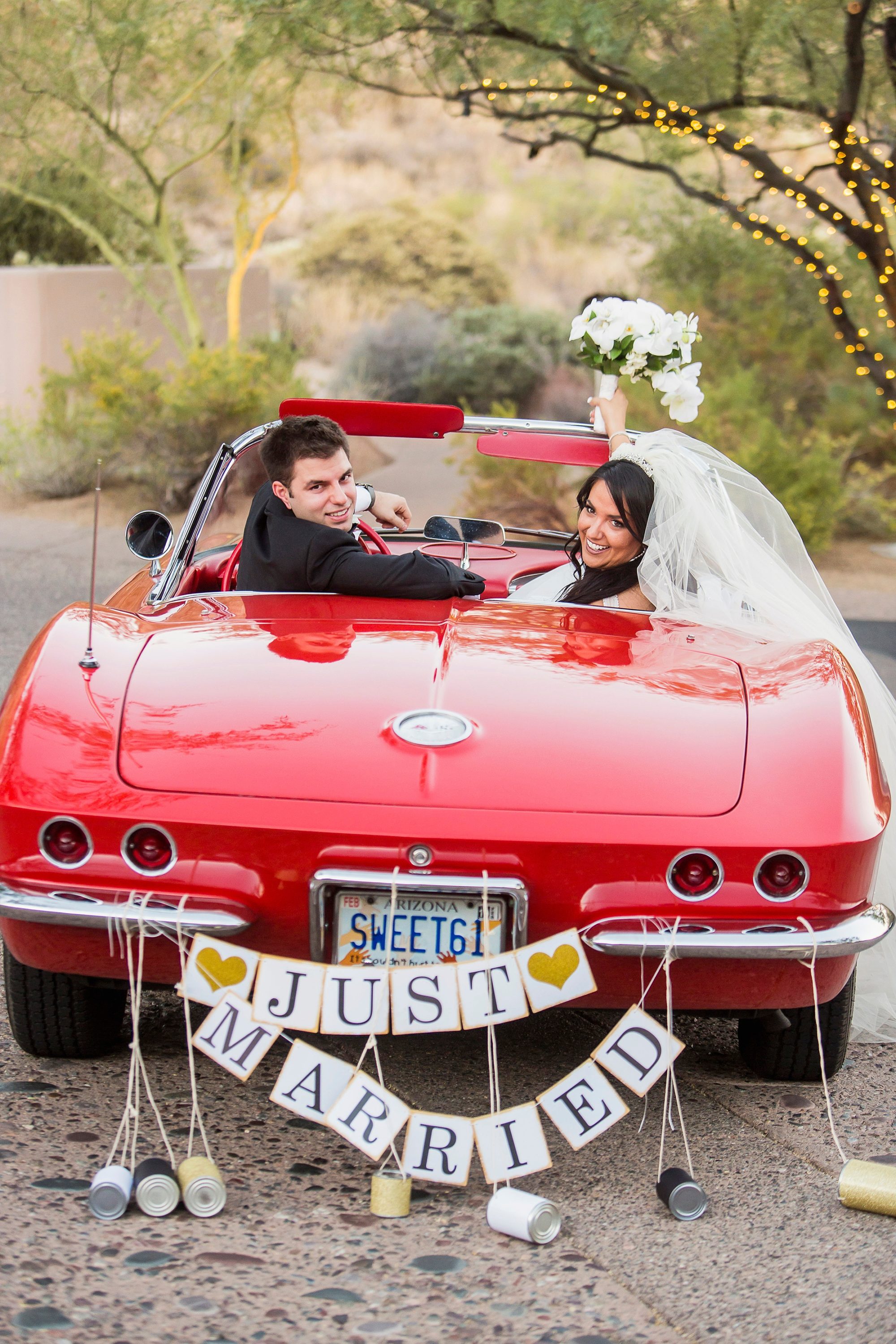 A couple raises their hands to cheer in their red classic car with a just married sign on their wedding day at Four Seasons Resort in Scottsdale