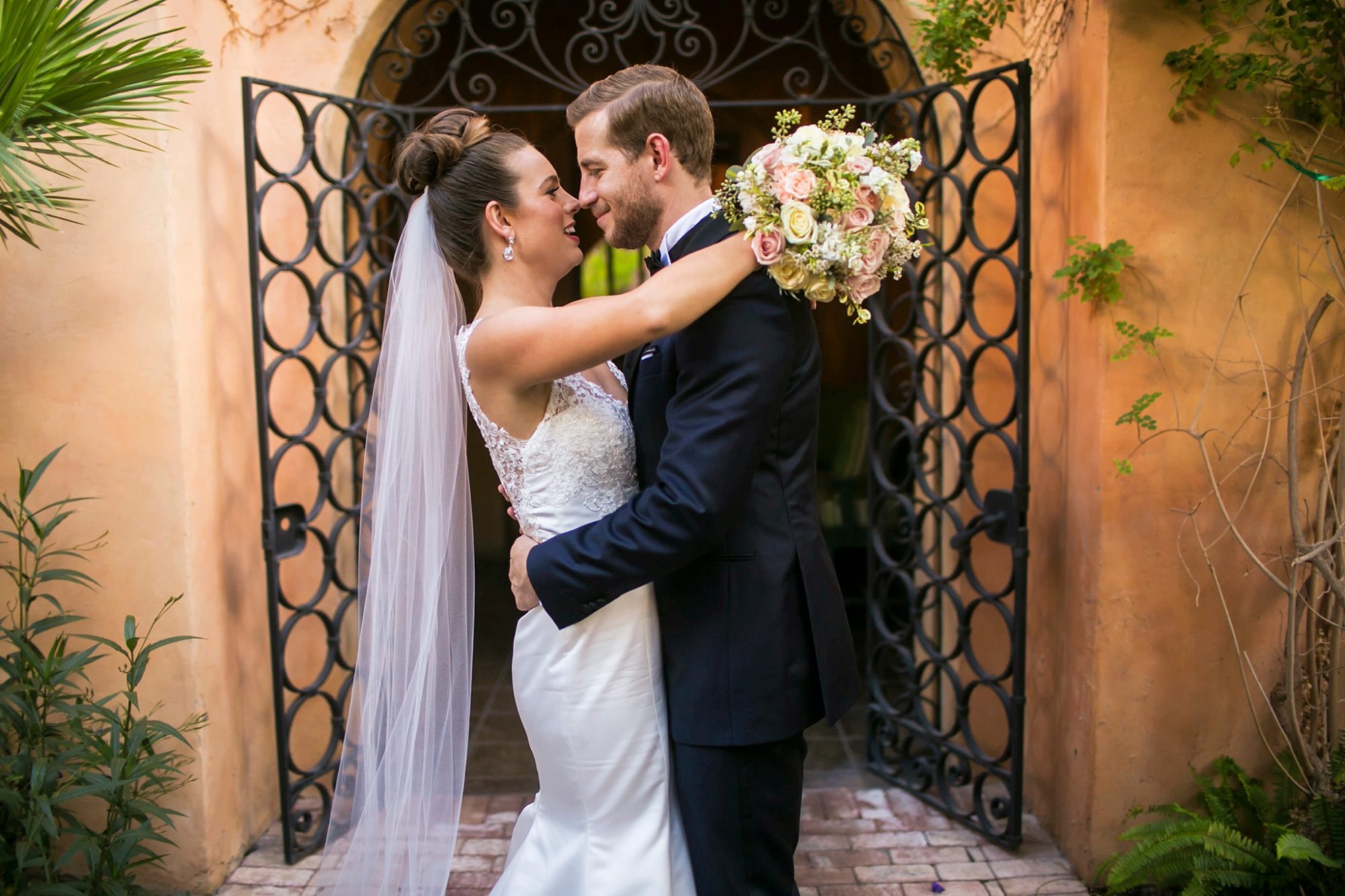 Royal Palms wedding with a bride and groom holding each other in font of an arch and decorative iron gates